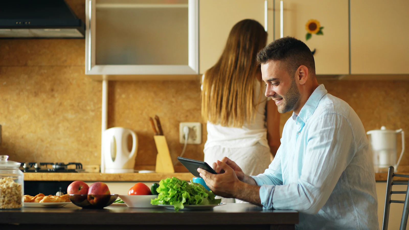 Couple in their kitchen, one reviewing a tablet at the table