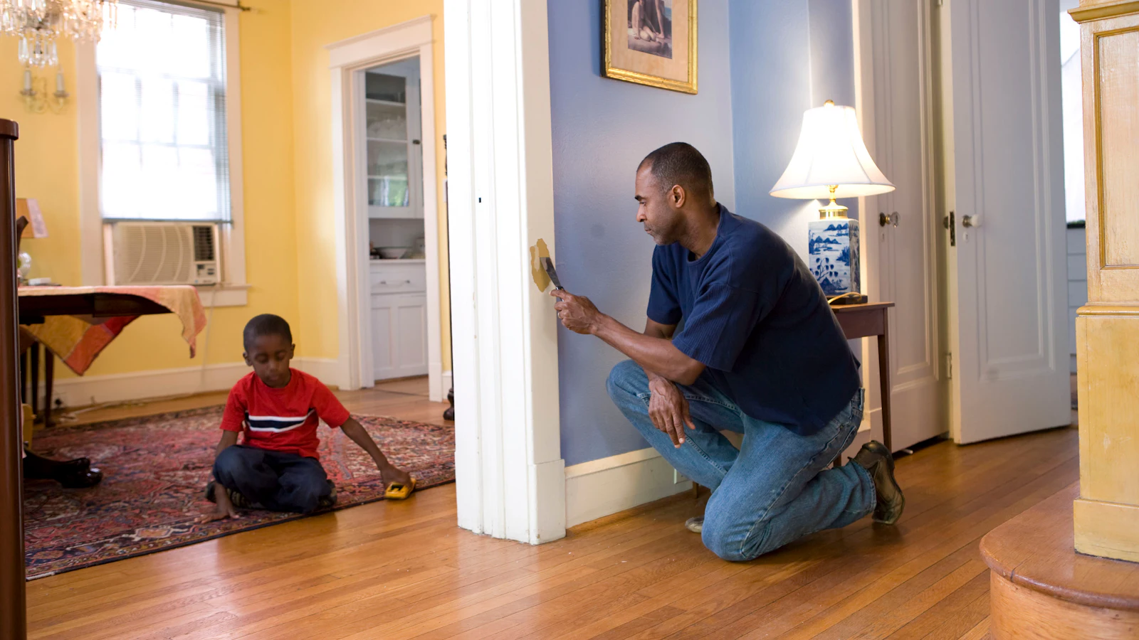 Technician kneeling to inspect a wall inside a family home