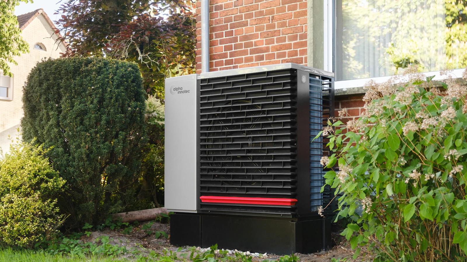 Outdoor heat pump unit beside a brick house and garden